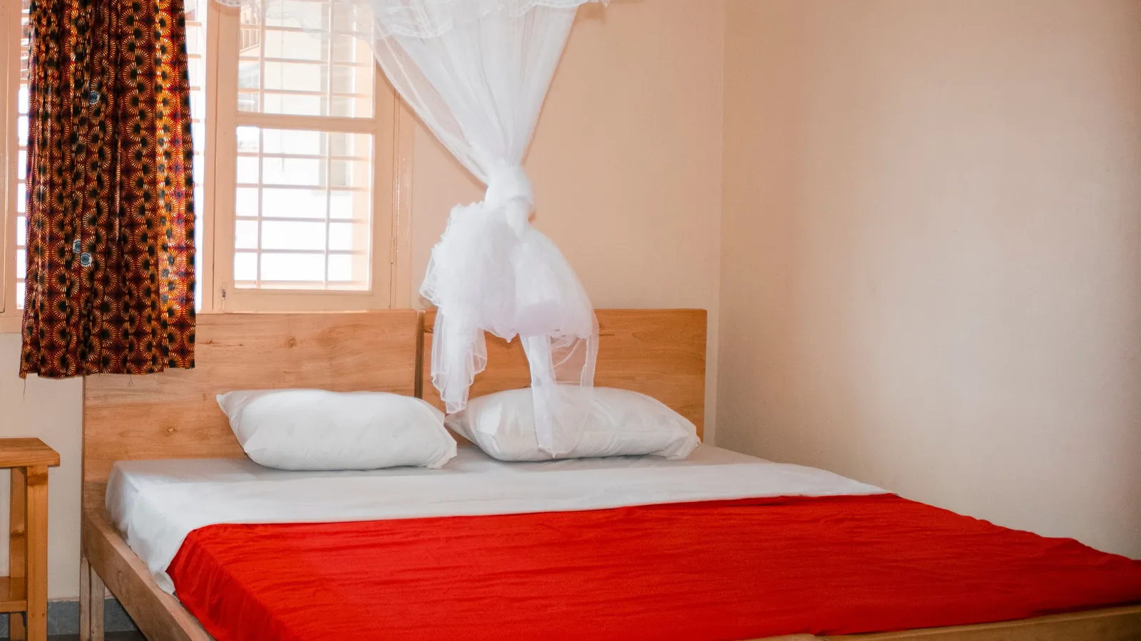 A bedroom in Kampala, Uganda: a mosquito net tied up over a wooden bed with a bright red blanket