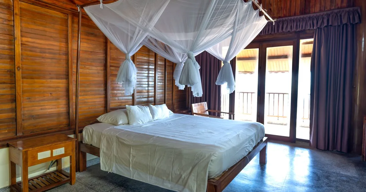 A bed draped with mosquito netting in a wooden room opening onto a veranda
