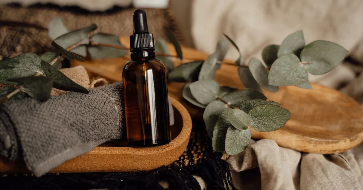 Amber glass dropper bottle of essential oil next to fresh eucalyptus branches on a plain surface
