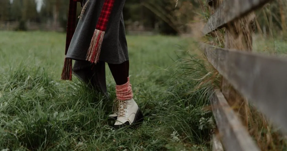 A person walking through tall grass in boots and outdoor clothing
