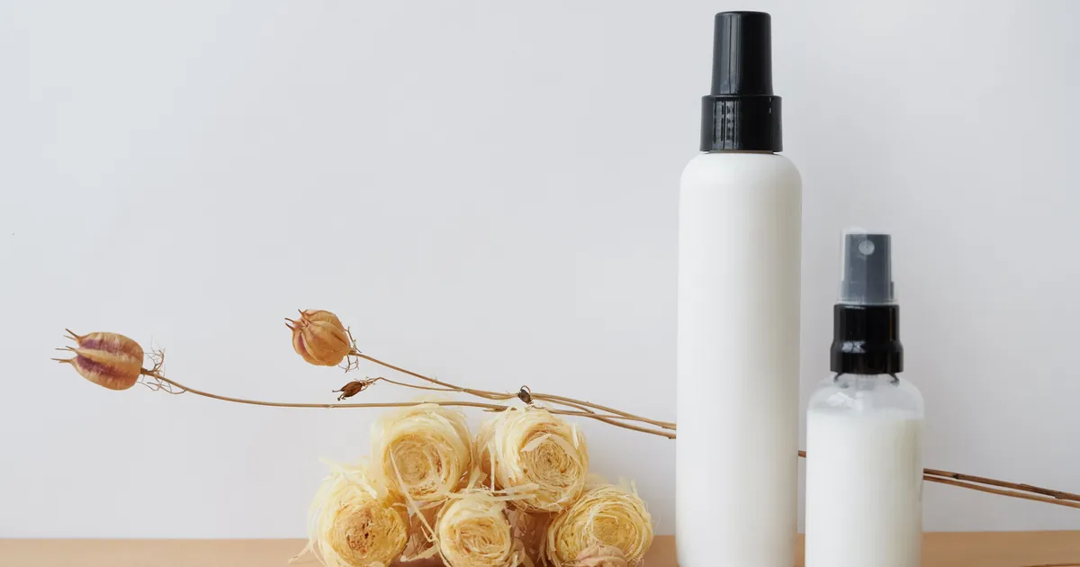 A white lotion bottle and a white spray bottle side by side on a warm background