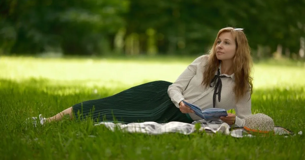 A person lying on a blanket reading on summer grass